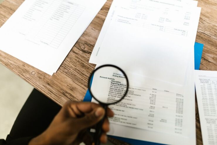 Close-up of hand using magnifying glass to review documents.