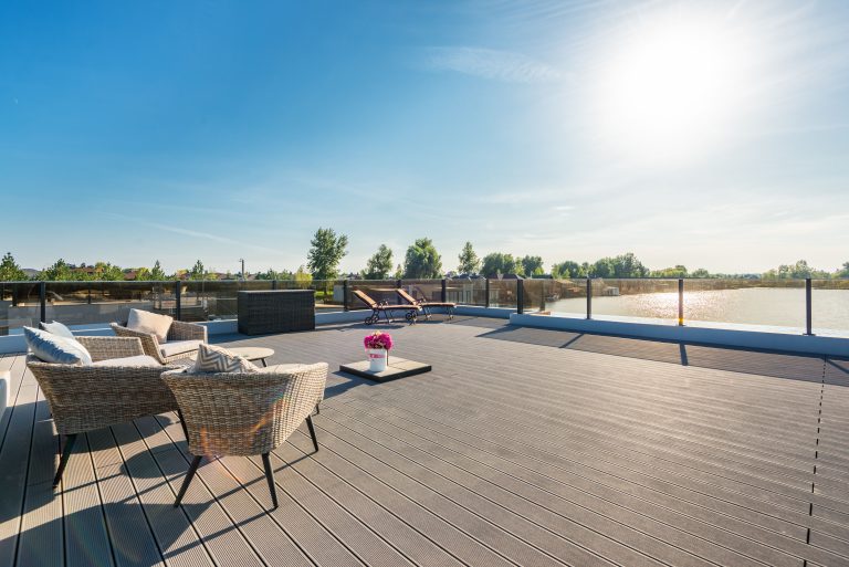 Spacious outdoor deck with rattan furniture and a lounging area under bright summer sun, illustrating a finished decking project.